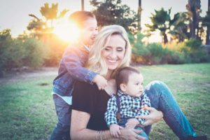 woman sits on the grass with two young boys