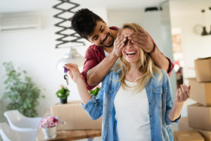 man covers woman's eyes as she holds keys to new home