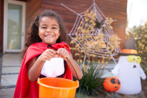 girl in cape holds orange bucket in front of halloween decorations