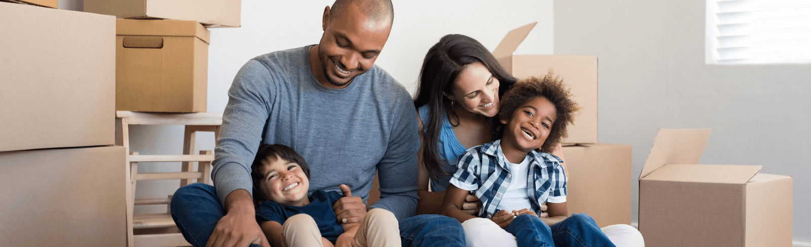 parents with two children sit on floor in front of packing boxes