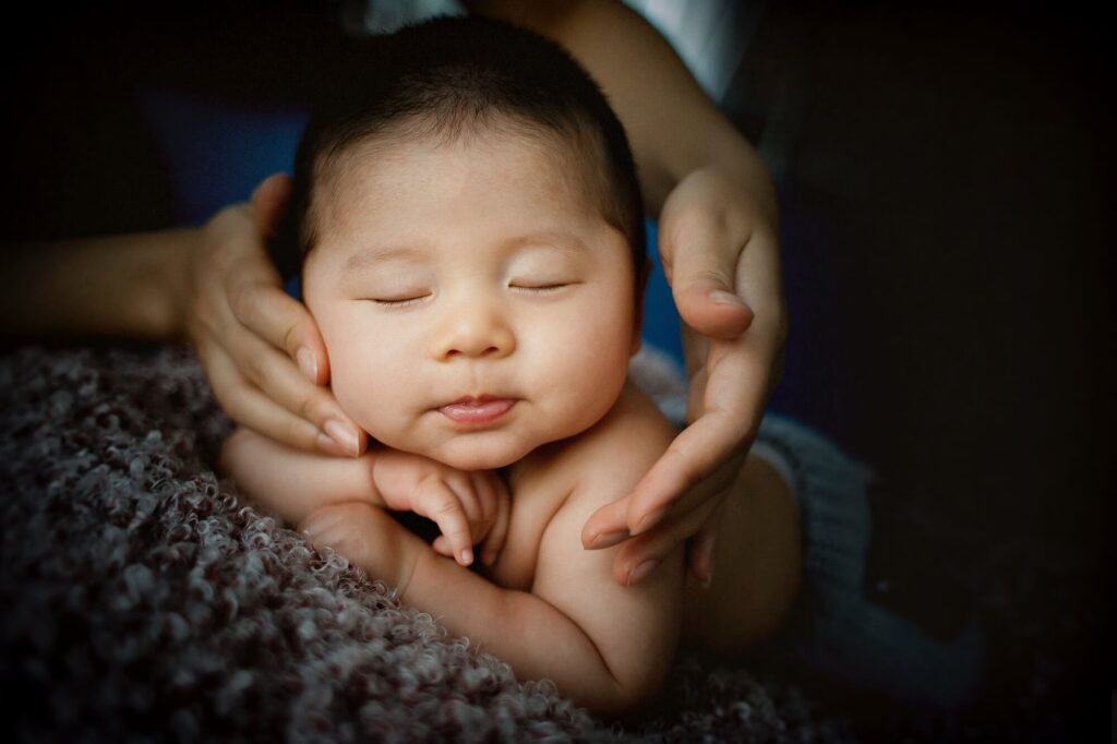 sleeping baby's face is framed by adult hands